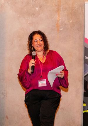 A lady talking holding a microphone and paper