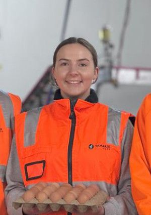 Three people smiling and holding a carton of eggs